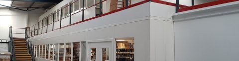 A view of a structural mezzanine floor installation within an industrial building, featuring a clean white partition wall.
