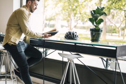 A person standing in a sunlit office next to a desk that holds a potted plant and a bicycle helmet.