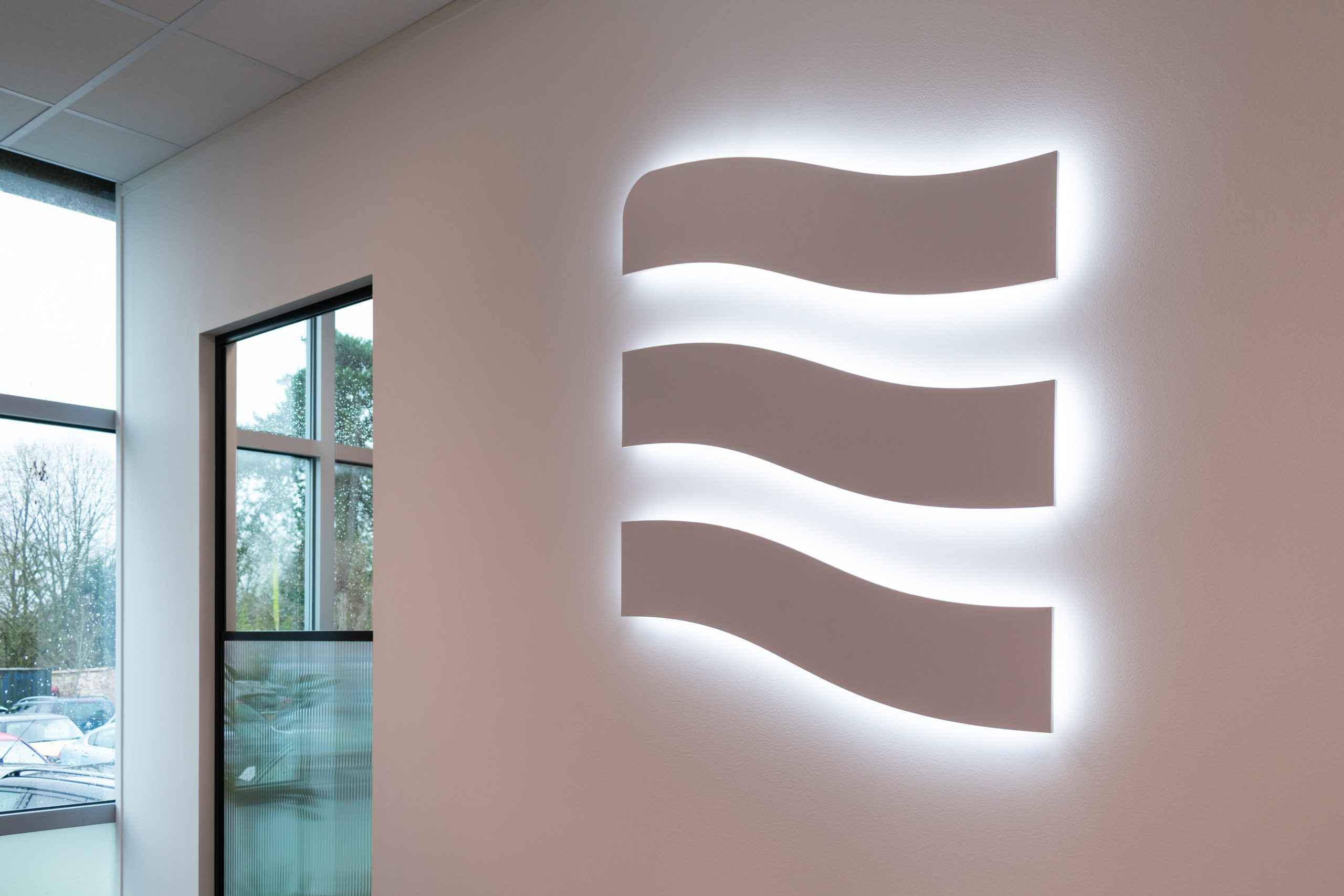 Illuminated brand logo displayed on a white office wall