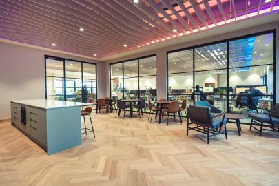 A spacious office lounge area featuring a blue island counter, wood flooring, and comfortable seating in a clean, open layout.