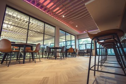 A canteen area within an office with tailored ceiling design, table and chirs and herringbone flooring.