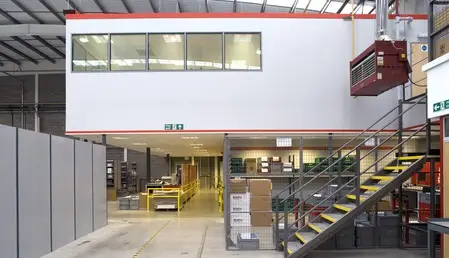 office mezzanine floor with staircase sitting above a warehosue with shelving and forklift below. 