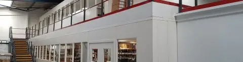 A view of a structural mezzanine floor installation within an industrial building, featuring a clean white partition wall.
