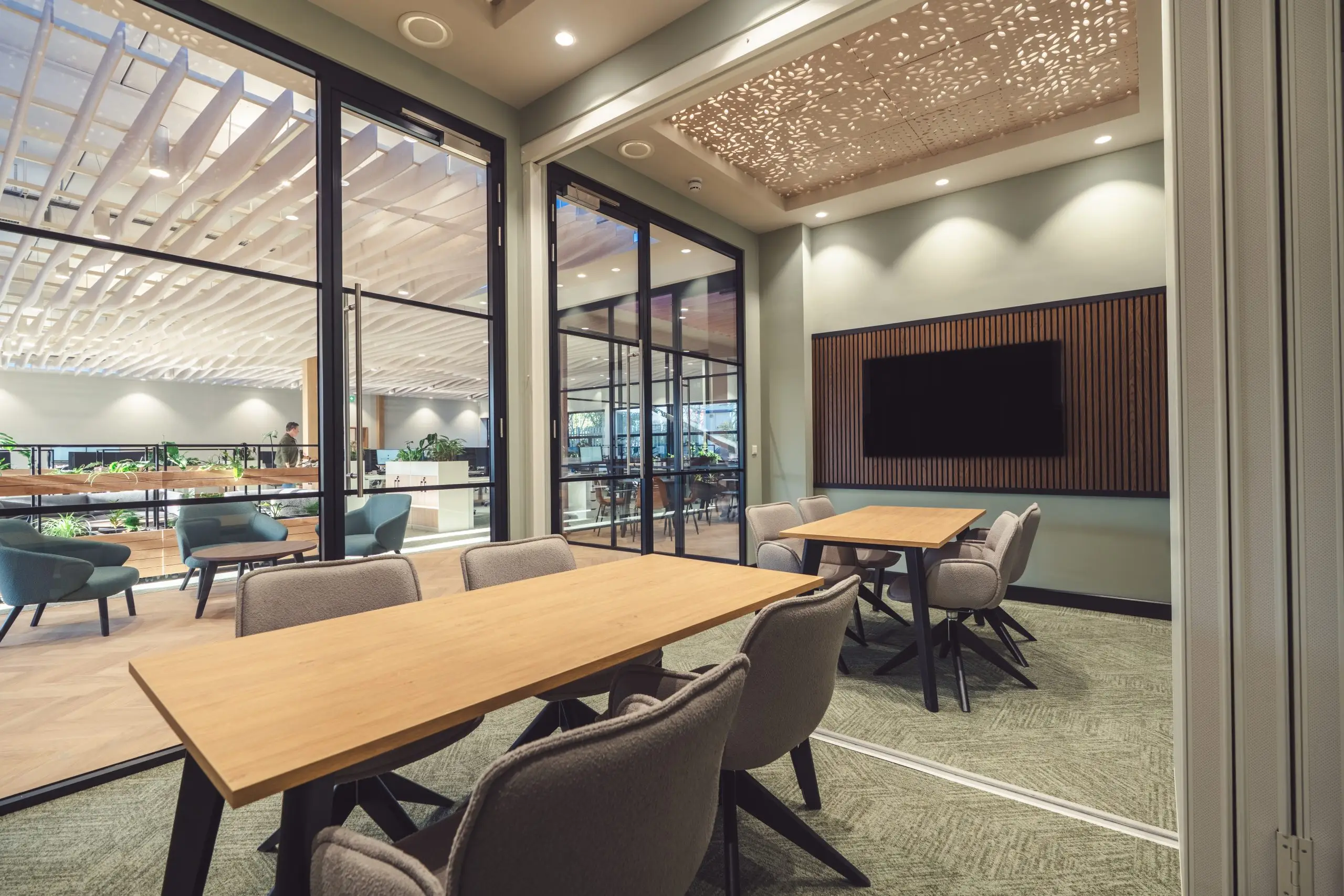 Flexible meeting space, image shows wooden desks, large panes of glass for light, and slatted wall finishes