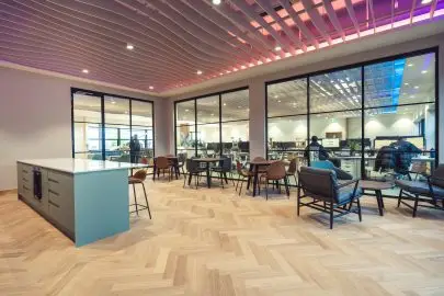 A spacious office lounge area featuring a blue island counter, wood flooring, and comfortable seating in a clean, open layout.
